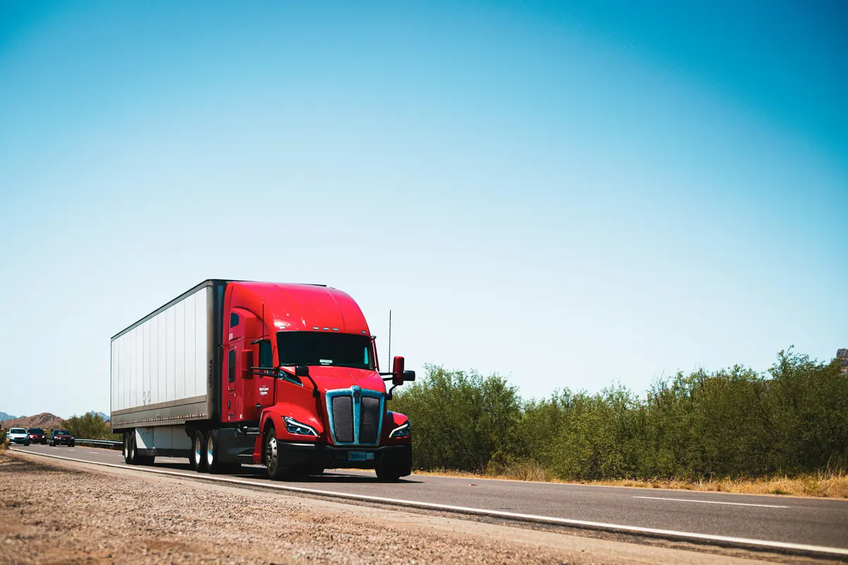 Red Kenworth T680 hauling a dry van trailer down a desert highway
