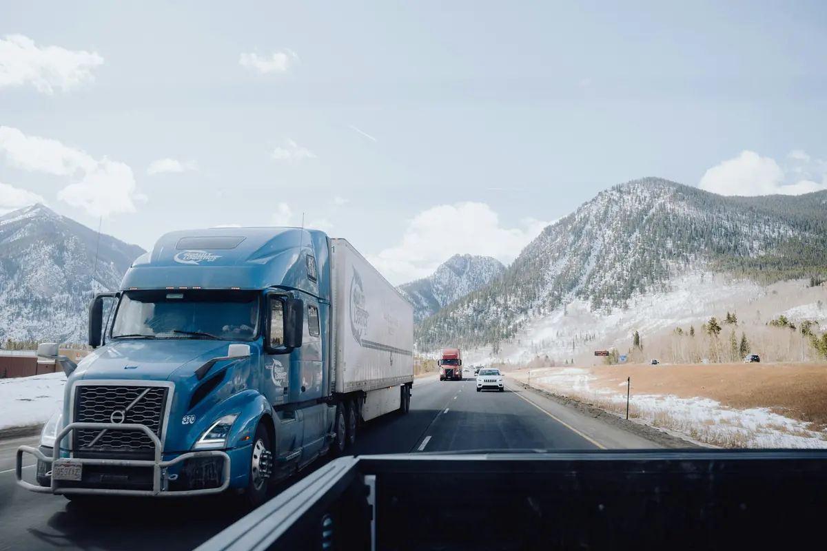 Blue Volvo VNL tractor pulling a dry van trailer through a snowy mountain pass