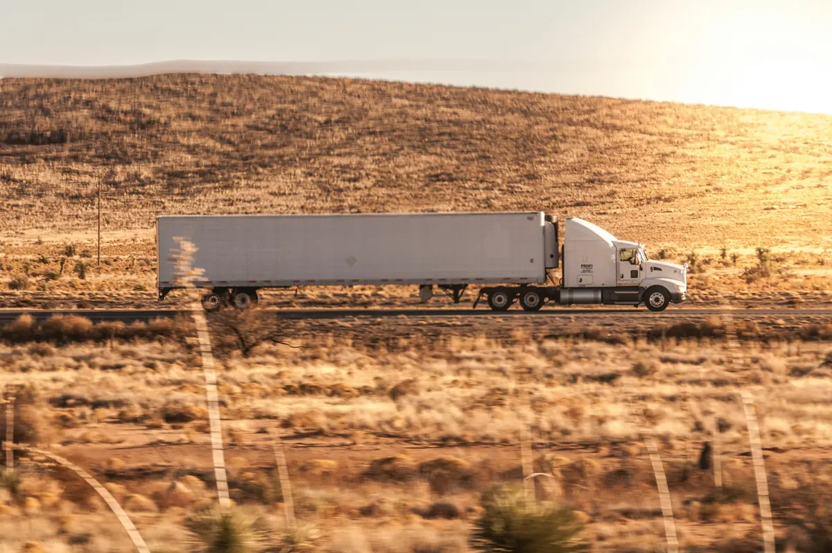 White Kenworth tractor and dry van trailer moving past open rangeland