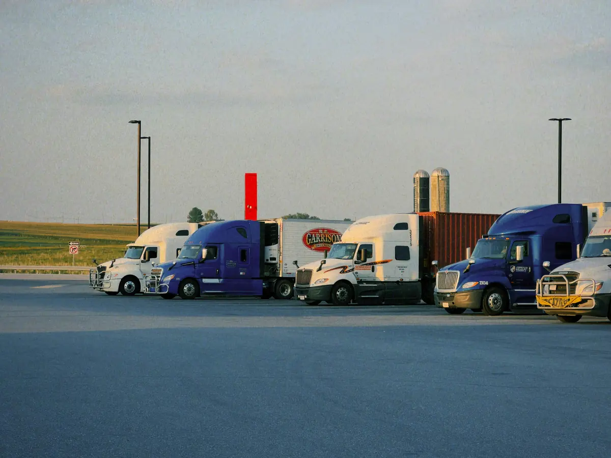 A row of Class 8 tractors parked side by side at a truck stop