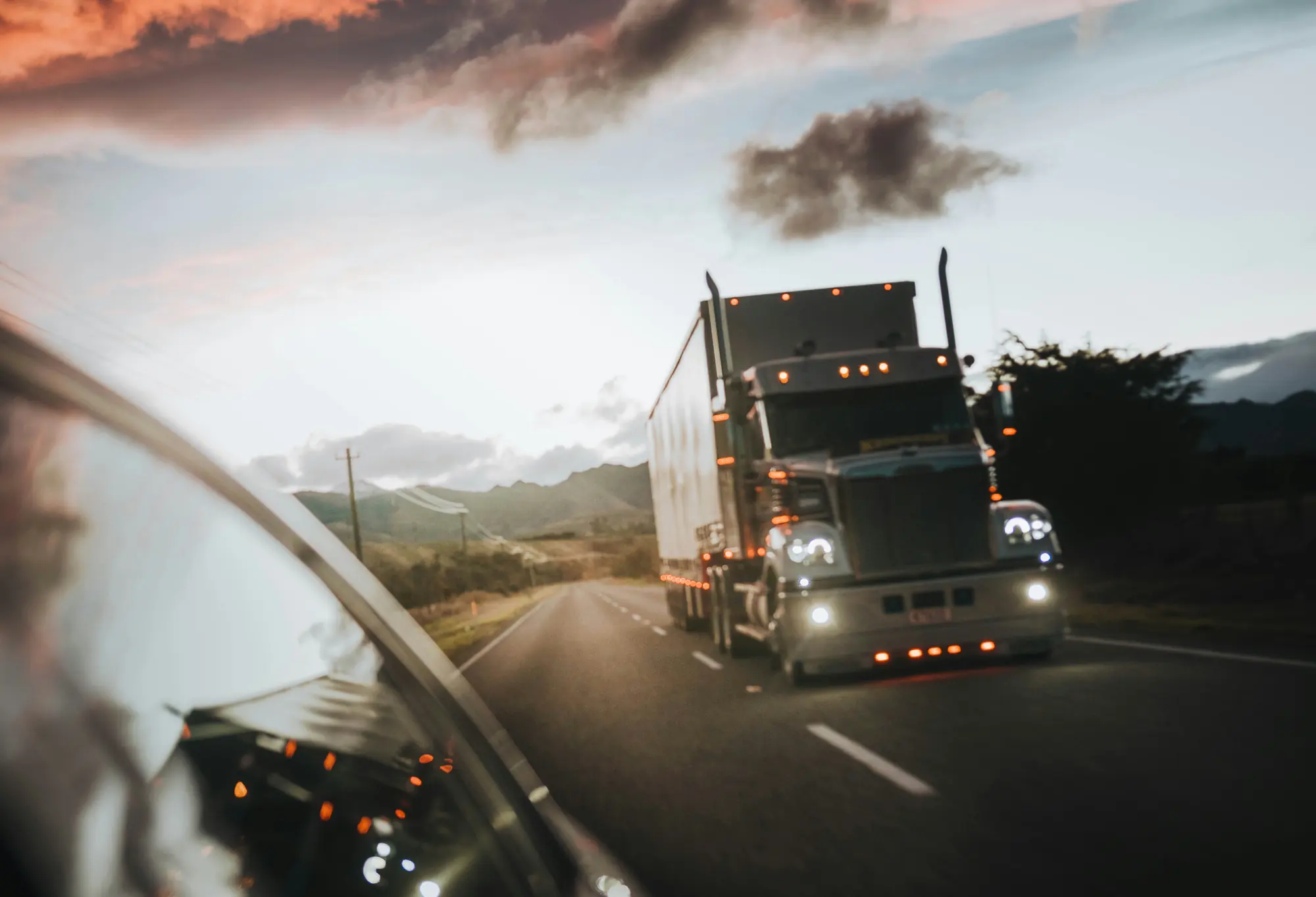 Tractor trailer running a highway at dusk under an orange sky