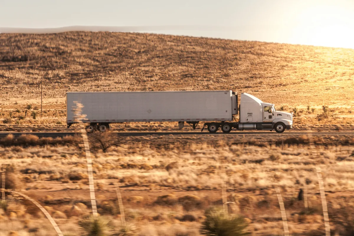 A tractor-trailer running down a desert highway at sunset.