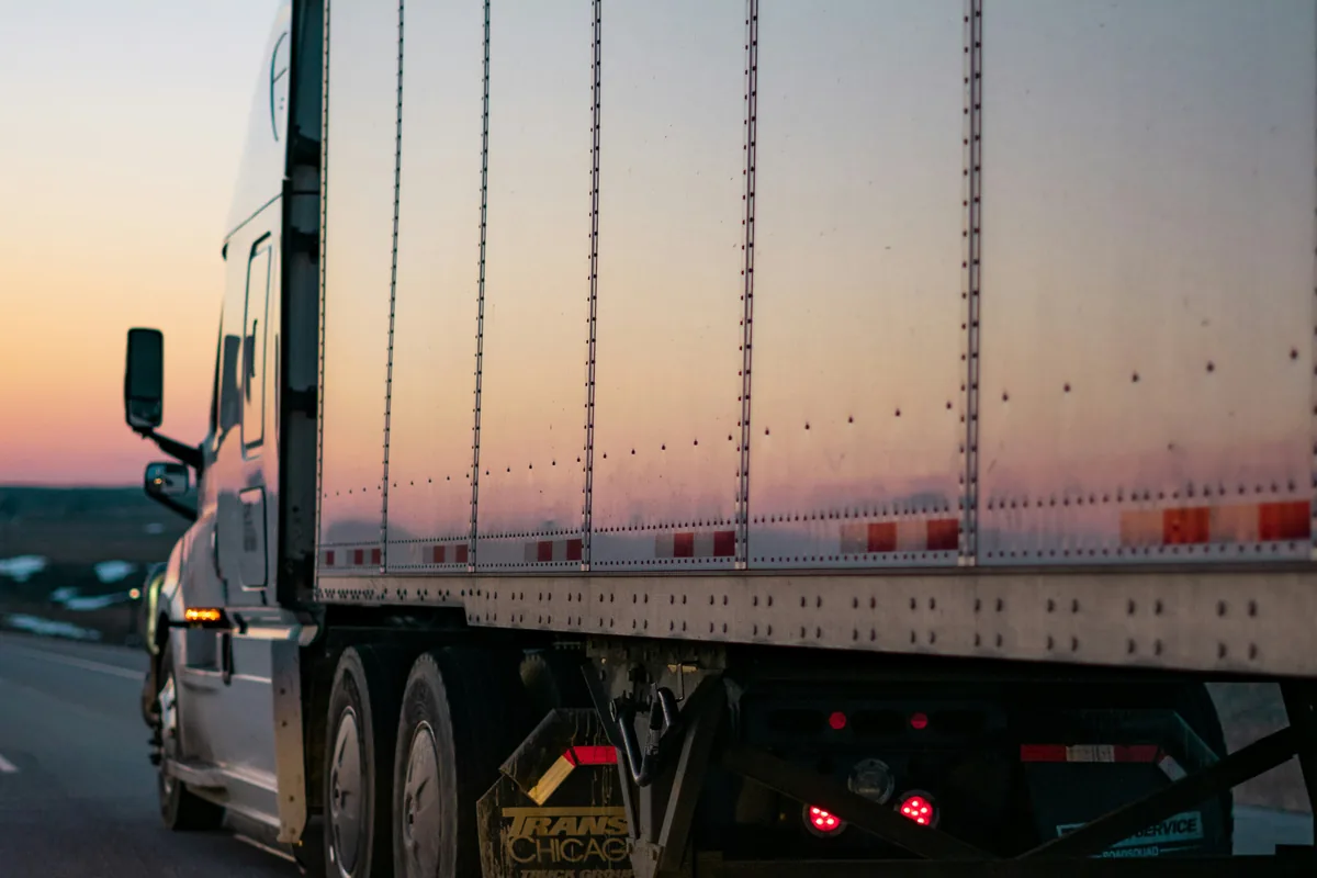 A tractor-trailer on the interstate at sunset.